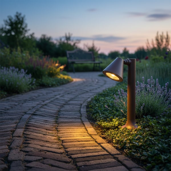 Eine moderne Gartenleuchte aus Metall beleuchtet einen geschwungenen Ziegelweg in einem bepflanzten Garten bei Dämmerung.