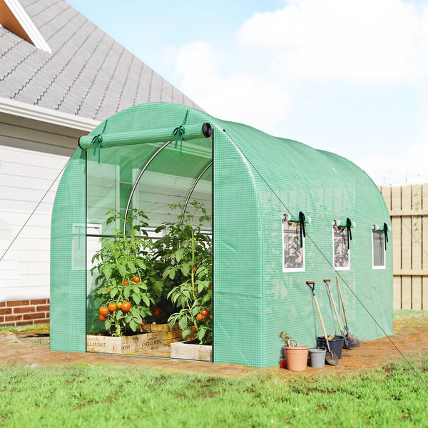Grünes Foliengewächshaus im Garten mit Tomatenpflanzen in Holzkisten, Gartengeräten und seitlichen Belüftungsfenstern.