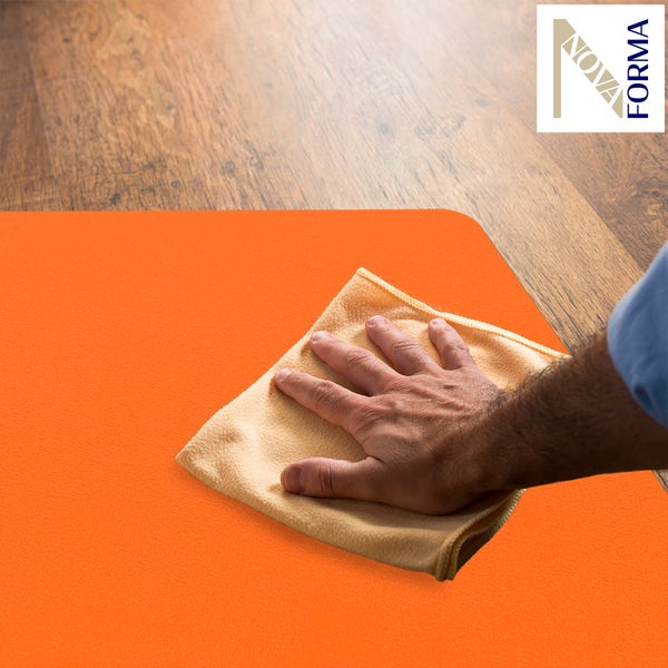 Eine Hand reinigt eine orangefarbene Bodenmatte mit einem weichen Tuch auf einem Holzboden. Nova Forma Logo.