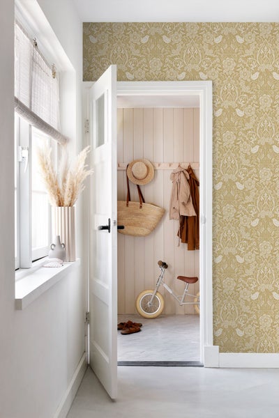 Vliestapete mit floralem Muster und Vögeln in Ocker und Weiß in einem hellen Flur mit offener weißer Tür.