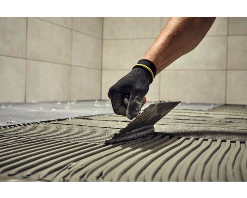 Fliesenleger trägt Kleber mit einer Kelle auf den Boden auf