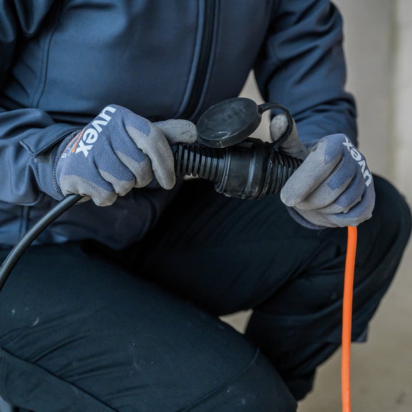 Eine Person in Arbeitskleidung und Uvex-Handschuhen verbindet ein Verlängerungskabel.