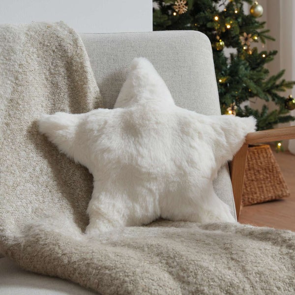 Dekoratives sternförmiges Kissen aus Fell auf einem Sessel mit Überwurfdecke und Weihnachtsbaum im Hintergrund