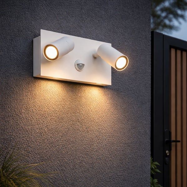 Moderne weiße Außenwandleuchte mit zwei verstellbaren LED-Strahlern und integriertem Bewegungsmelder an einer strukturierten Fassade.