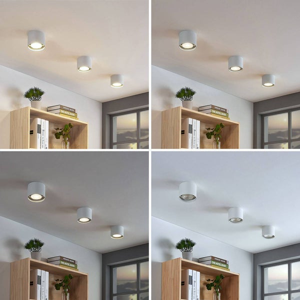 Drei weiße zylindrische Aufbaustrahler an einer Zimmerdecke über einem Holzregal in einem hellen Raum.