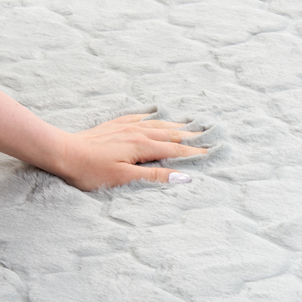 Hand streicht über einen weichen Teppich aus Kunstfell mit Strukturmuster.
