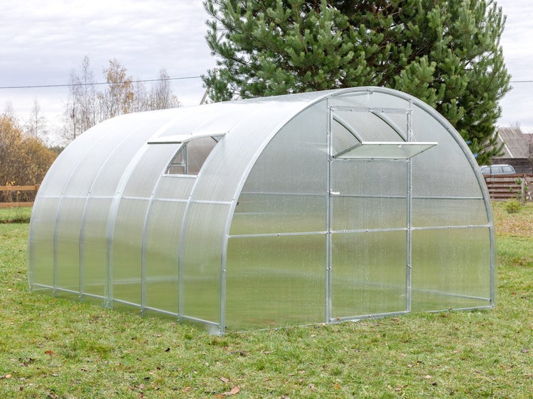 Rundbogengewächshaus aus Polycarbonat mit Metallrahmen, einer Tür und zwei Belüftungsfenstern auf einer Rasenfläche.
