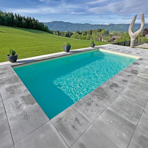 Moderner Außenpool mit grauen Terrassenplatten, Pflanzgefäßen und Blick auf eine Hügellandschaft.