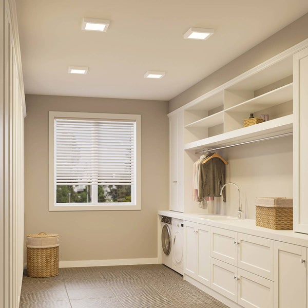 Heller Waschraum mit weißen Schränken, Waschmaschine und vier quadratischen LED-Einbauleuchten an der Decke für gleichmäßige Beleuchtung.