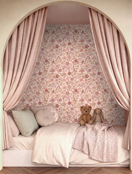 Kinderbett in einer Bogennische mit floral gemusterter Tapete, gerafften Vorhängen, Kissen, Strickdecke, Teddybär und Stoffhase.