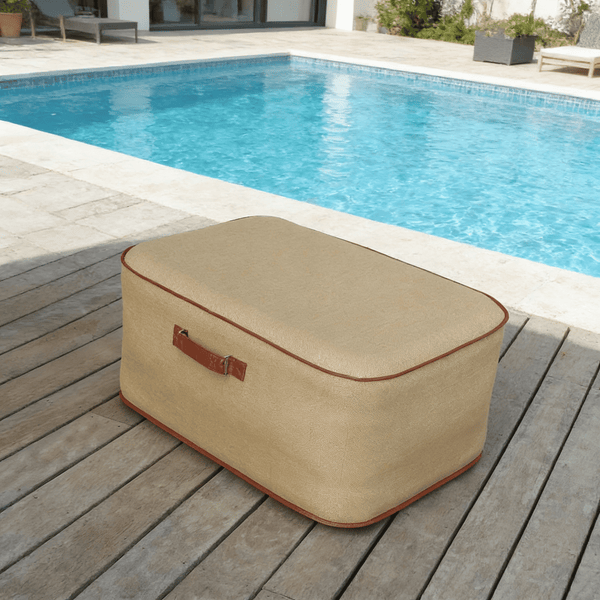 Beigefarbenes, rechteckiges Sitzkissen mit Ledergriff auf einer Holzterrasse neben einem hellen Swimmingpool.