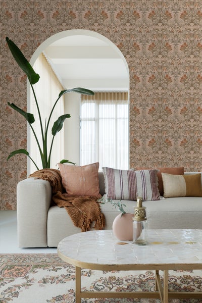 Wohnzimmer mit beiger Couch, Kissen, Decke, Tisch und floraler Tapete für eine gemütliche Atmosphäre