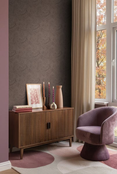 Wohnzimmer mit brauner gemusterter Tapete, Holzkommode, Kerzen, Dekoration und Sessel