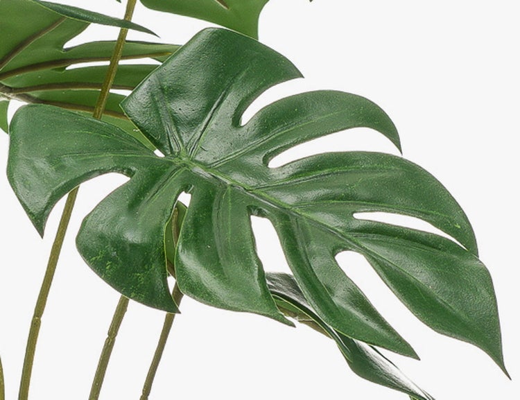 Detailaufnahme eines grünen künstlichen Monstera-Blattes mit charakteristischen Einschnitten und Löchern an dünnen Stielen.