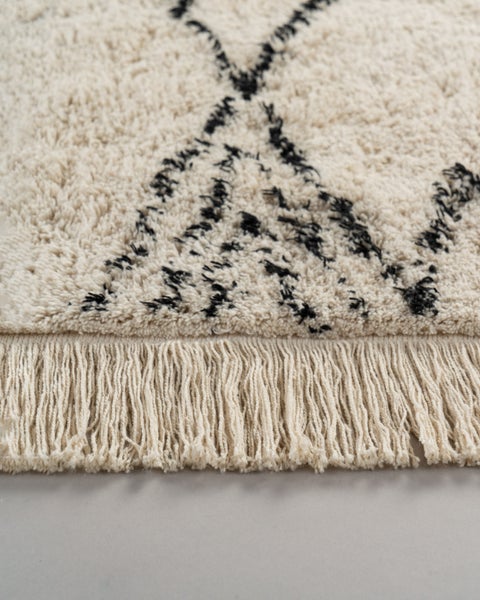 Hochflor-Teppich im Berber-Stil in Cremeweiß und Schwarz mit geometrischem Muster und Fransen.