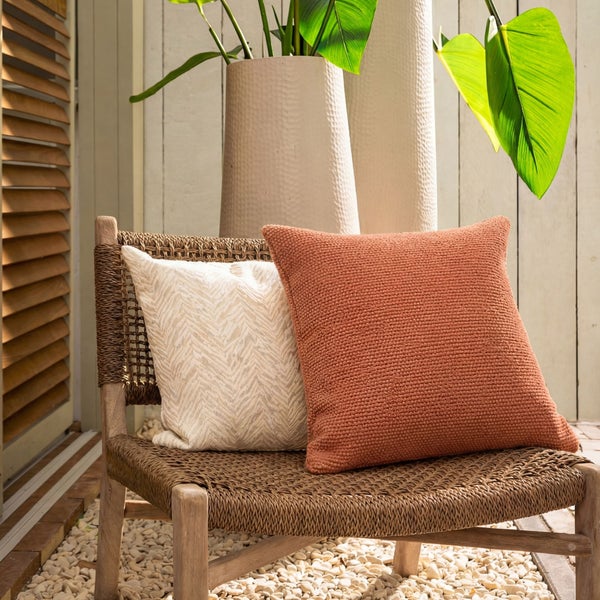 Dekorative Kissen auf einem Korbstuhl neben Pflanzen in Töpfen