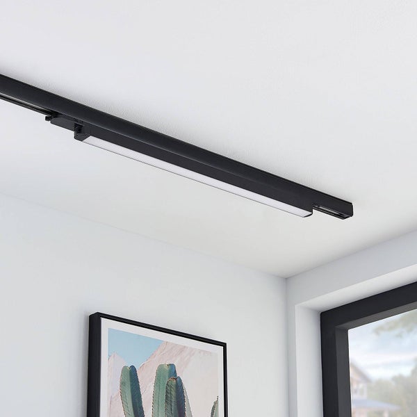 Schwarze lineare LED-Leuchte montiert an einem Schienensystem an einer weißen Decke in einem hellen Innenraum.