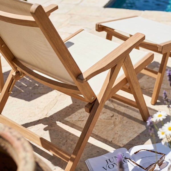 Hölzerner Gartenstuhl mit heller Textilbespannung und passender Fußablage auf einer Steinterrasse an einem Pool.