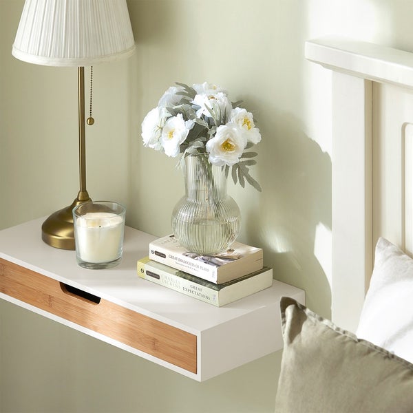 Dekoratives Schlafzimmer mit Lampe, Kerze, Blumen in Vase und schwebendem Nachttisch