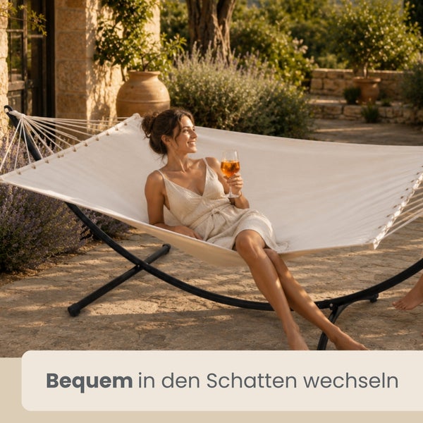 Hängematte mit Metallgestell auf einer hellen Steinterrasse im Garten mit einer entspannten Frau.