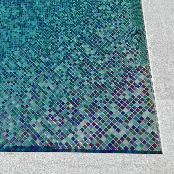 Schwimmbecken ausgekleidet mit quadratischen Mosaikfliesen in verschiedenen Blau- und Grüntönen mit einer umgebenden hellen Steinumrandung
