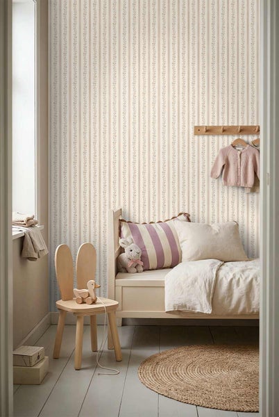 Helles Kinderzimmer mit floral gestreifter Tapete, einem Holzbett mit Kissen, einem hasenförmigen Stuhl und einem runden Juteteppich.