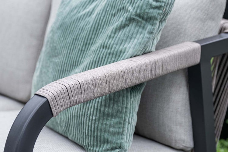 Nahaufnahme einer Gartenstuhl-Armlehne aus schwarzem Metall mit Seilumwicklung sowie ein grünes Cordkissen und graue Polster.