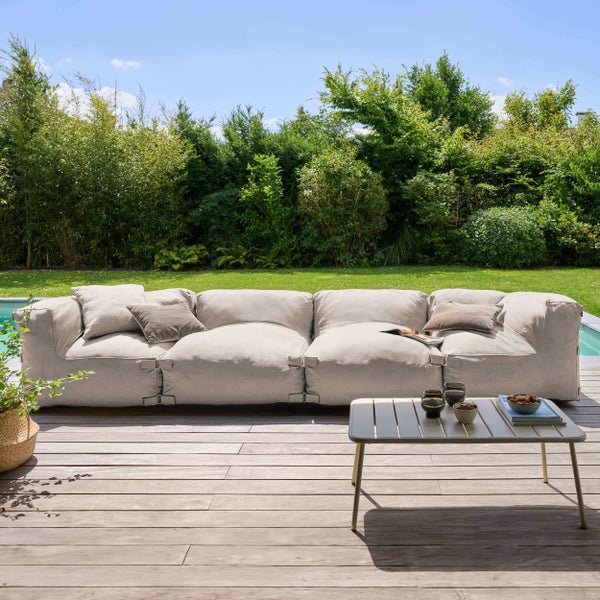 Modernes beiges Outdoor-Lounge-Sofa auf einer Holzterrasse neben einem Pool und einer grünen Gartenhecke, inklusive kleinem Metall-Beistelltisch.