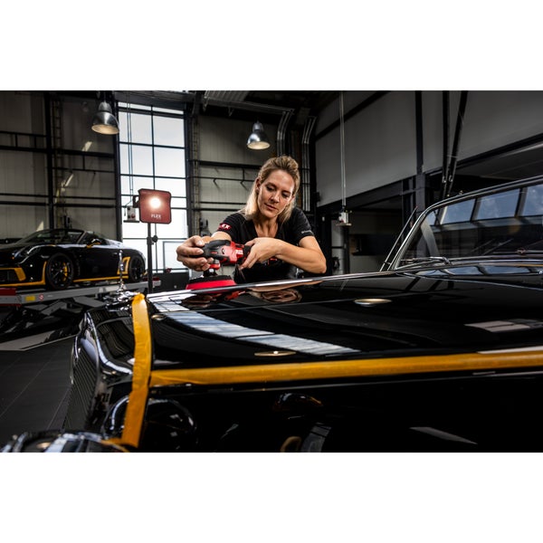 Eine Person poliert fachmännisch die Motorhaube eines schwarzen Oldtimers mit einem Flex Poliermaschinen Set in einer professionellen Werkstatt.
