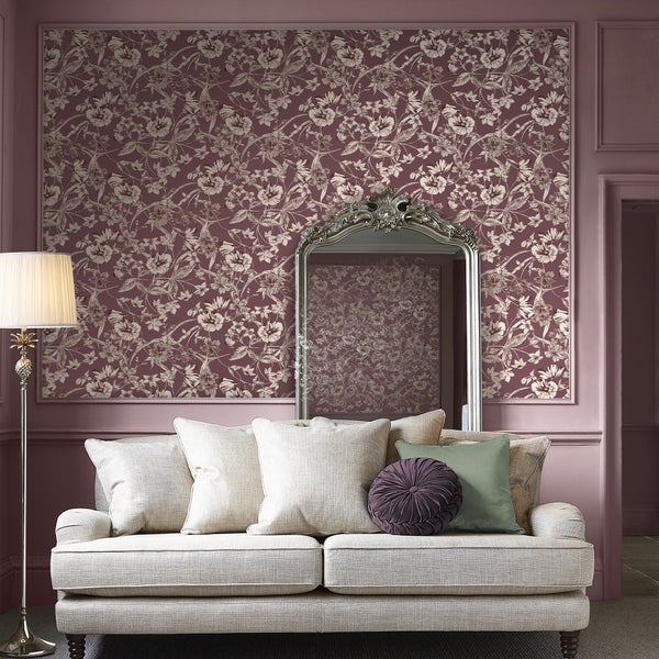 Wohnraum mit einer Wand, die mit einer floralen Tapete tapeziert ist, davor ein klassisches Sofa mit Kissen und ein großer silberner Wandspiegel.