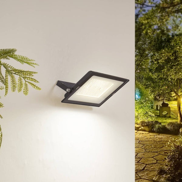 Schwarzer LED-Außenstrahler an weißer Wand montiert, beleuchtet einen Garten bei Nacht.