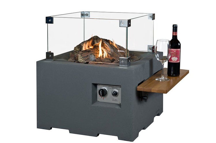 Quadratischer Gas-Feuertisch in Beton-Optik mit Glas-Windschutz, Holz-Seitenablage und dekorativen Holzscheiten über brennenden Flammen.