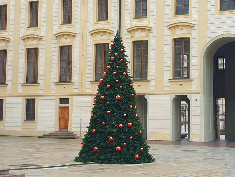Großer künstlicher Weihnachtsbaum mit roten Weihnachtskugeln vor der historischen Fassade eines Gebäudes im Außenbereich.