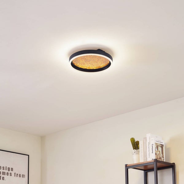 Runde LED-Deckenleuchte mit schwarzem Rahmen und strukturierter, goldfarbener Mitte an einer weißen Decke in einem hellen Raum.