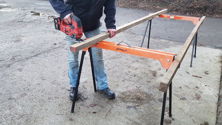 Person sägt Holzbrett mit Stichsäge auf einem Sägebock