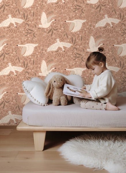 Szene mit einem Kind, das auf einem Bett vor einer Tapete mit Schwanmotiv sitzt
