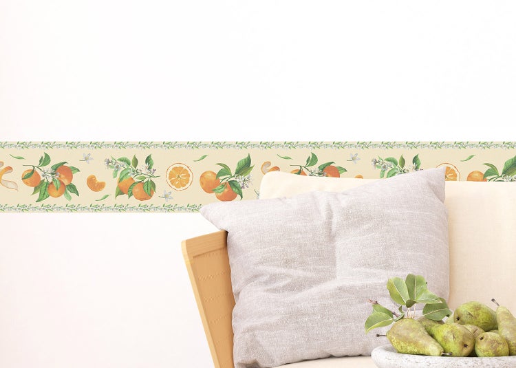 Selbstklebende Tapetenbordüre mit Orangen-Motiv und grünen Blättern an einer hellen Wand über einem Sofa.