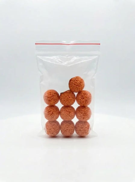 Zehn orangefarbene Filterbälle aus porösem Material in einem transparenten Druckverschlussbeutel.