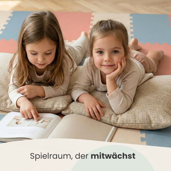 Zwei Kinder liegen auf einer bunten Puzzlematte und Kissen in einem hellen Spielzimmer und schauen in ein Buch.