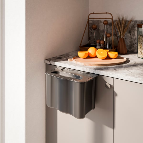 Bio-Mülleimer zum Einhängen an der Küchenschranktür, moderne helle Küche mit Marmor-Arbeitsplatte und Orangen auf einem Holzbrett.