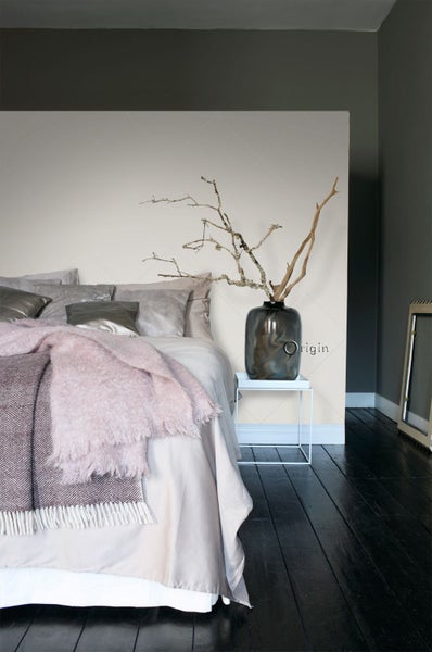 Schlafzimmer mit Bett, Kissen, Decken, Vase und Zweigen auf einem Nachttisch.