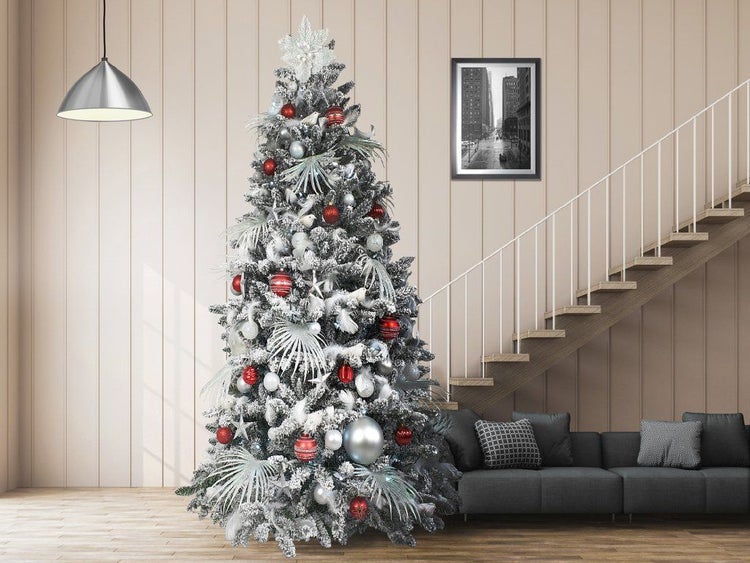 Geschmückter künstlicher Weihnachtsbaum mit Schneeoptik, dekoriert mit roten und silbernen Weihnachtskugeln im Wohnzimmer neben einer Treppe.