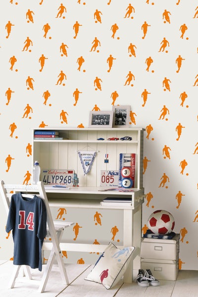 Dekoratives Kinderzimmer mit Schreibtisch, Stuhl, Fußball und Accessoires vor einer Tapete mit Fußballmotiven.