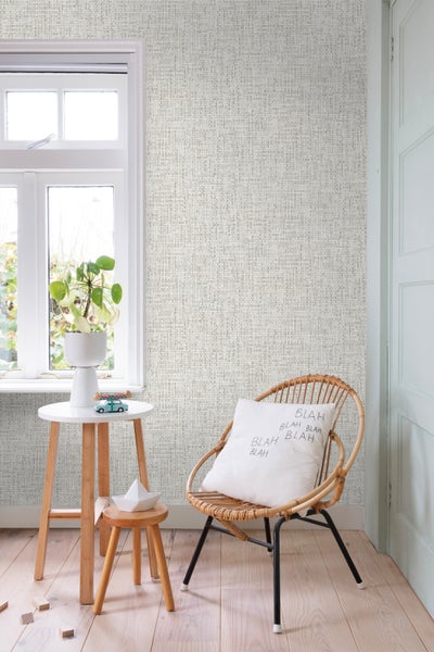 Szene mit Textiltapete, Rattansessel, Beistelltisch und Dekoration in einem Zimmer.