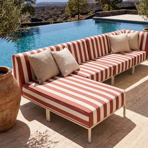 Modernes Lounge-Sofa für den Außenbereich mit gestreiften Polstern und Kissen auf einer Terrasse neben einem Pool.