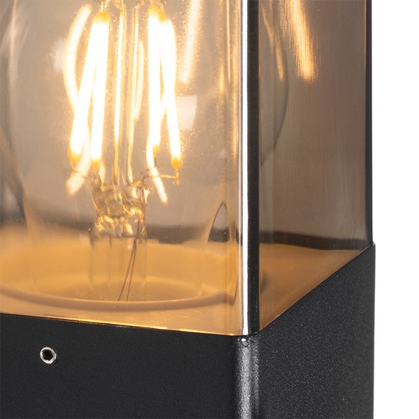 Nahaufnahme einer Außenlampe mit sichtbarem LED-Filament-Leuchtmittel im quadratischen Glasgehäuse mit schwarzem Metallfuß.