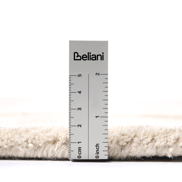 Beliani Logo auf einem Lineal zur Messung der Florhöhe eines hellen Teppichs in Zentimetern und Inches.