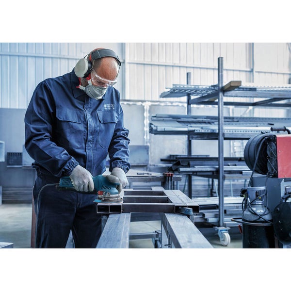 Ein Handwerker schleift mit einer Schleifmaschine ein Metallgestell, während er Schutzkleidung trägt.