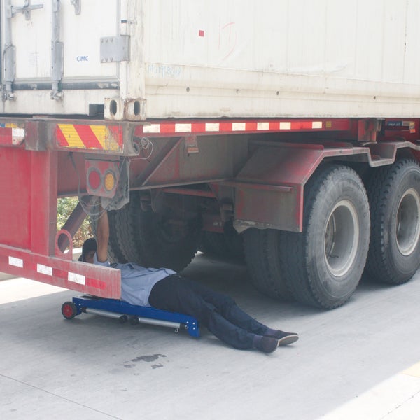 Person auf einem blauen Montagerollbrett bei Wartungsarbeiten unter einem Lastkraftwagen.