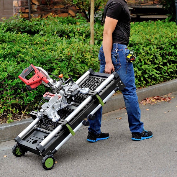 Eine Person zieht eine mobile Werkbank mit montierter Kappsäge auf Rollen im Außenbereich.